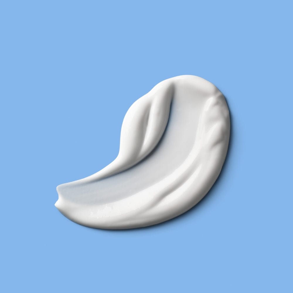 A small, crescent-shaped white cream smear with visible texture and thickness on a blue surface.