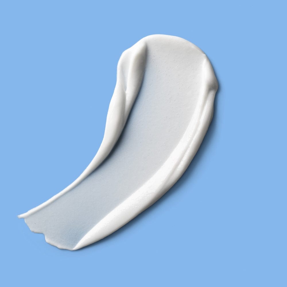 A wide, curved streak of white cream with soft peaks and a smooth texture, shown against a blue backdrop.
