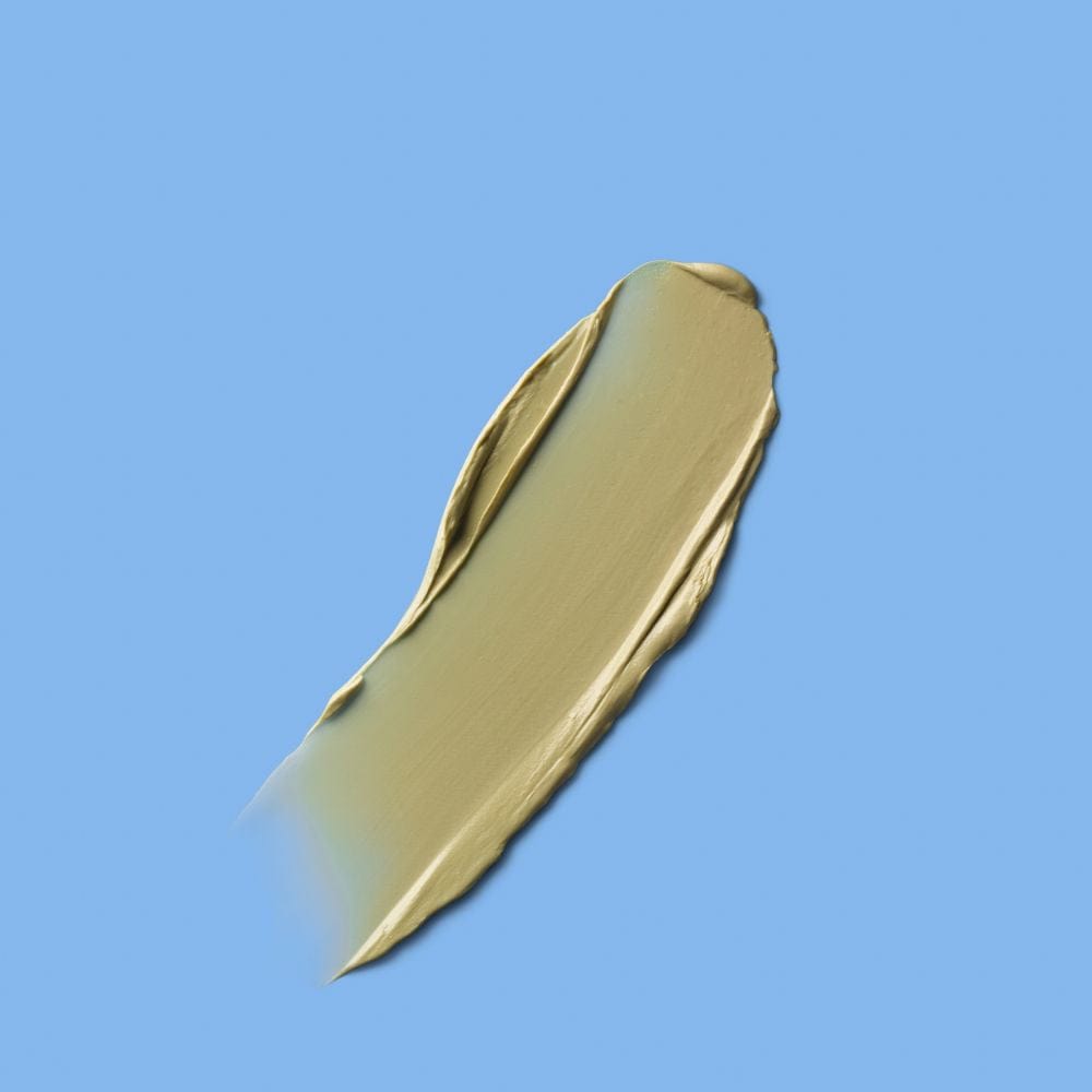 A single smooth swipe of light olive-green cream or mask product against a solid blue background, showing glossy texture and even application.