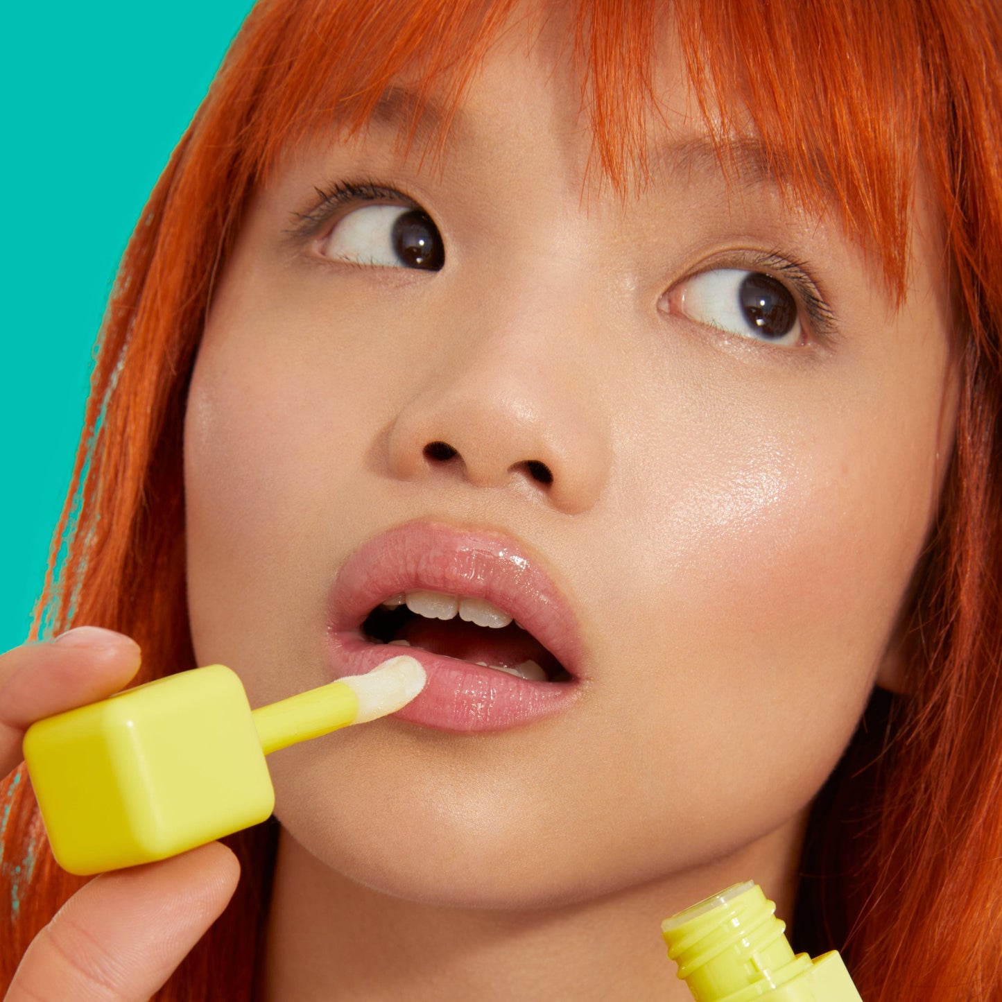 An Asian girl with red hair appying a BYOMA liptide to her lips.