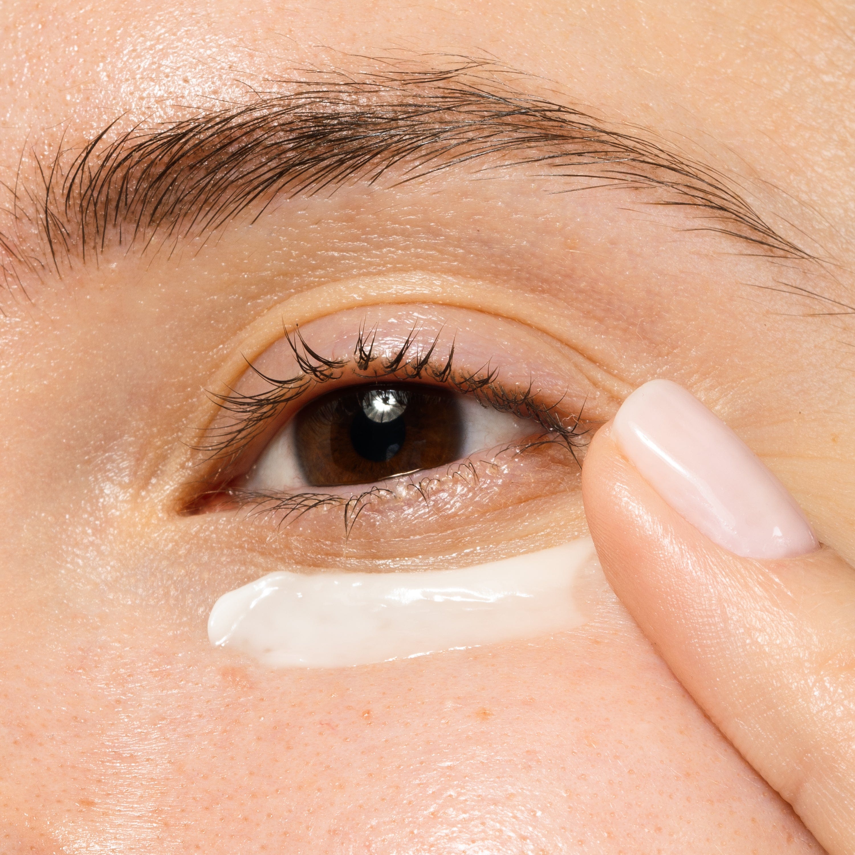 Closeup of a person applying an eye cream with her finger tips.