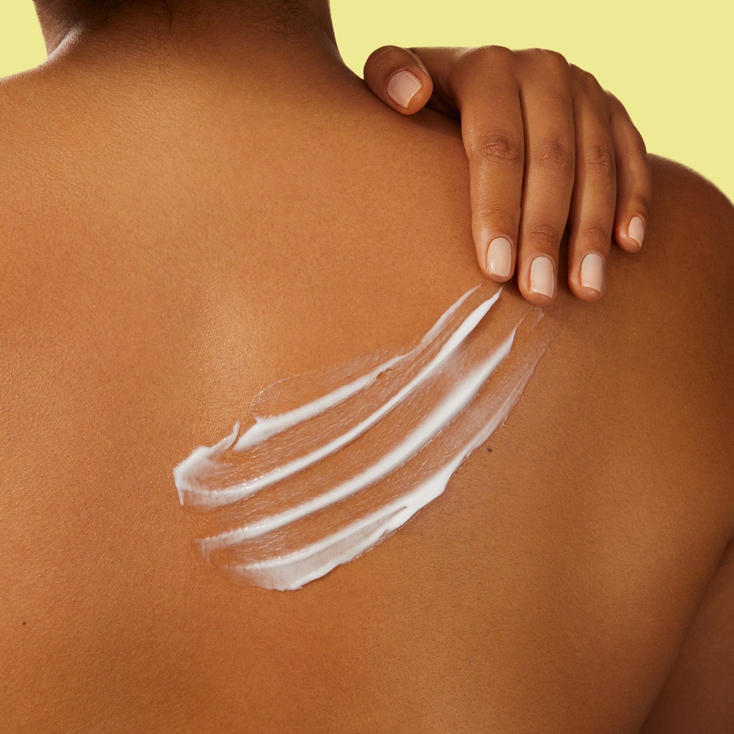 A woman's back with her hands on her shoulder and cream on her back.