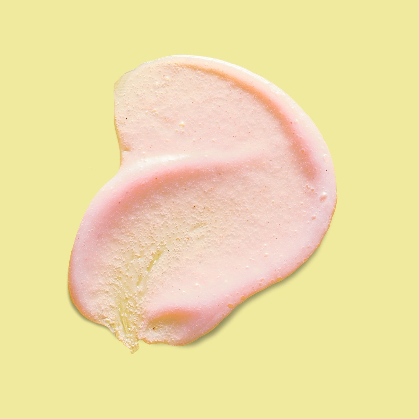A peach coloured cream with granules applied on a yellow surface.