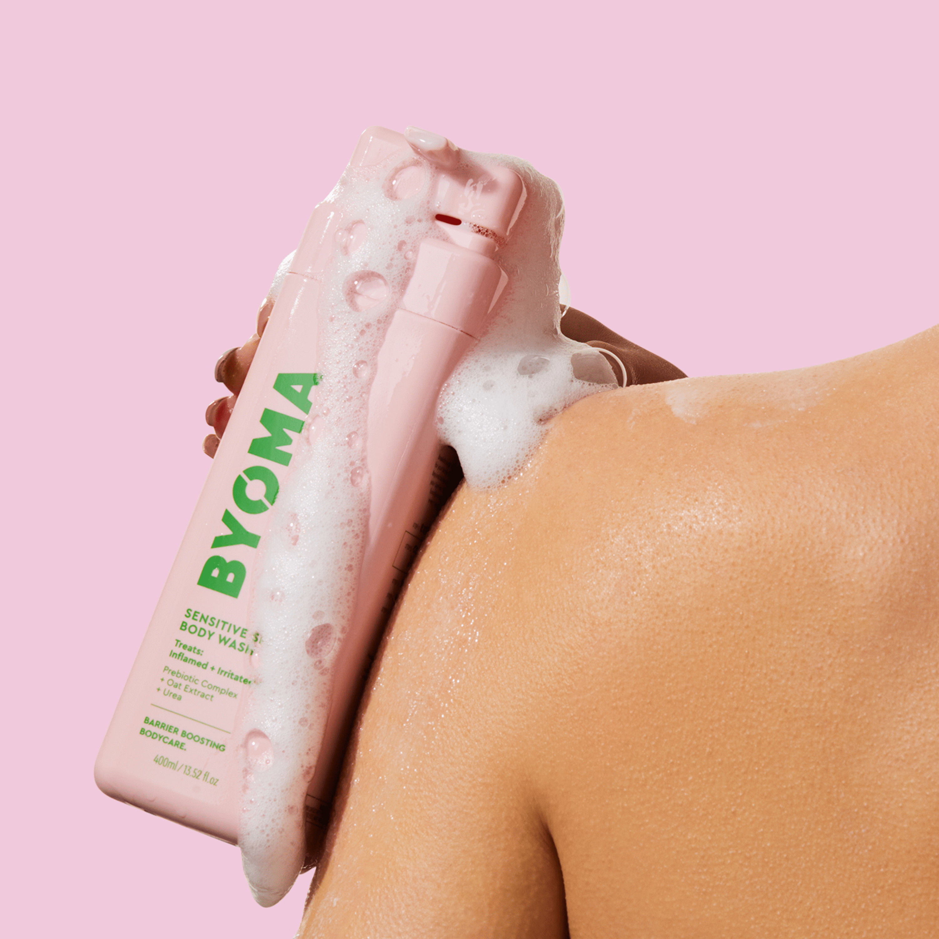 A woman holding a lathered BYOMA SENSTIVE BODY WASH on her shoulder from the back.