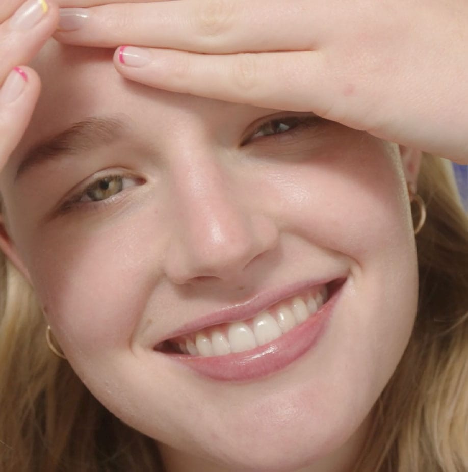 Closeup of a smiling girl with hands on her forehead.