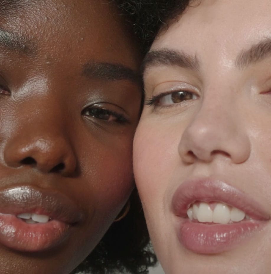 Image of black and white girls with heads touching each other and smile on their lips.