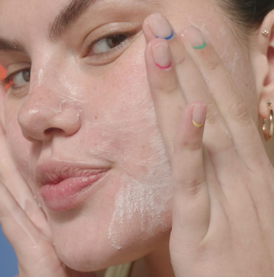 A white woman applying cleanser with her hands on her face and puckered lips.