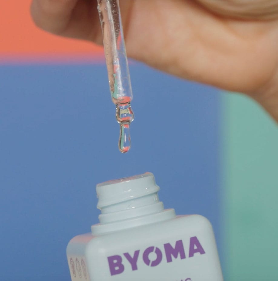 Closeup of a dropper with product dropping off it and a BYOMA white bottle.