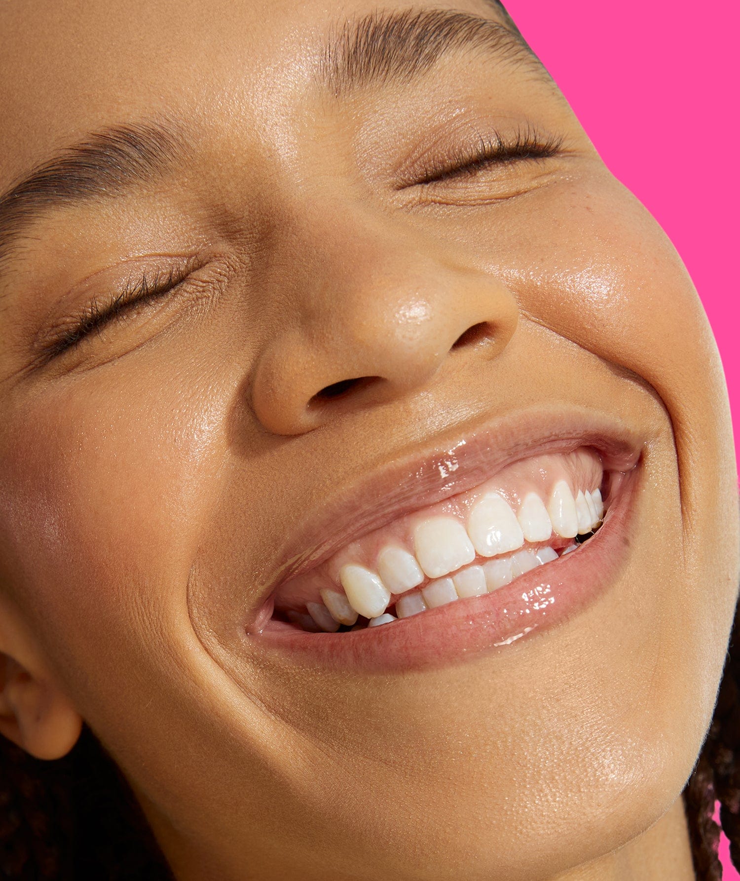 A girl closing her eyes, looking upwards and smiling. She is wearing a transparent lip gloss.