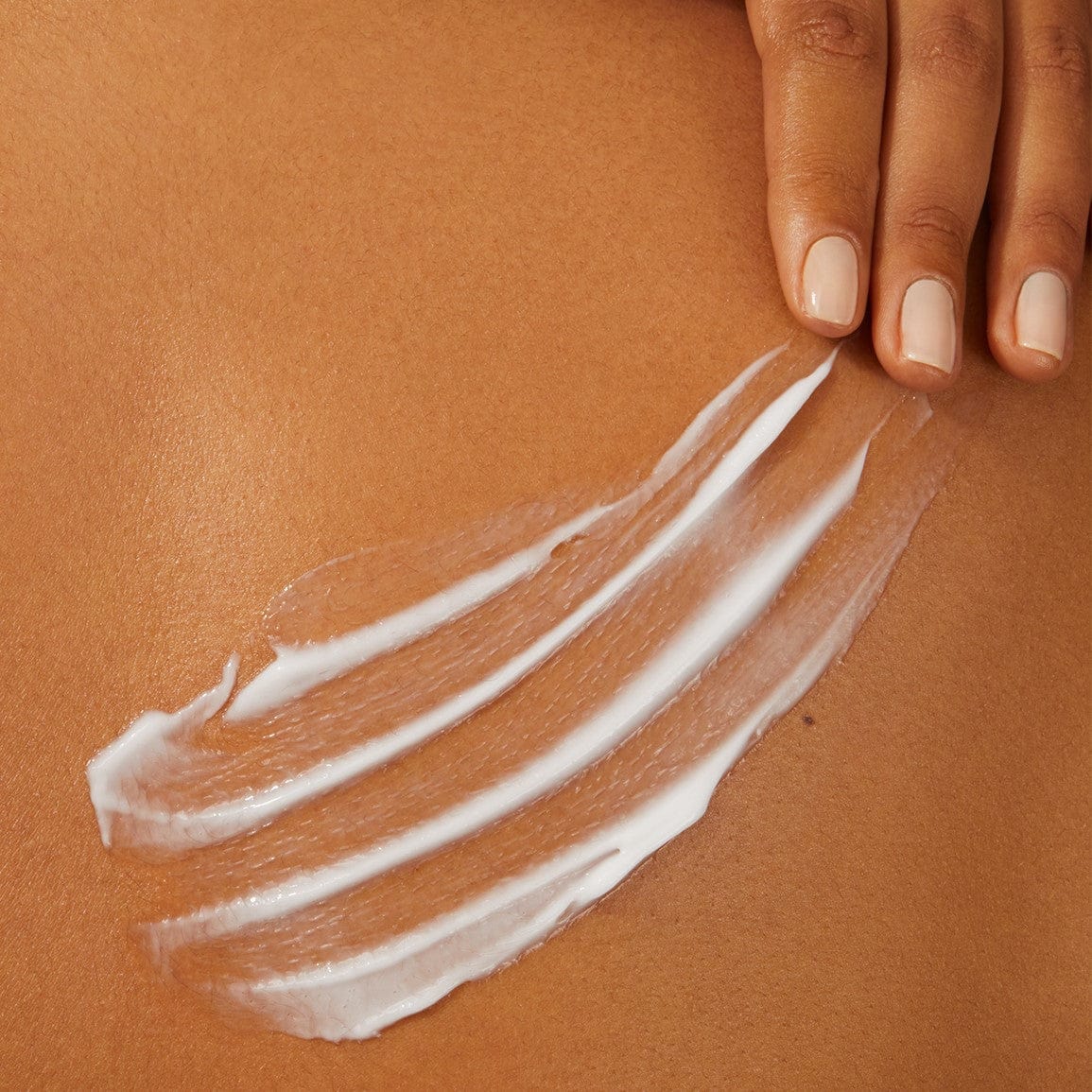 White lotion spead over the body with three fingers and manicured nails.